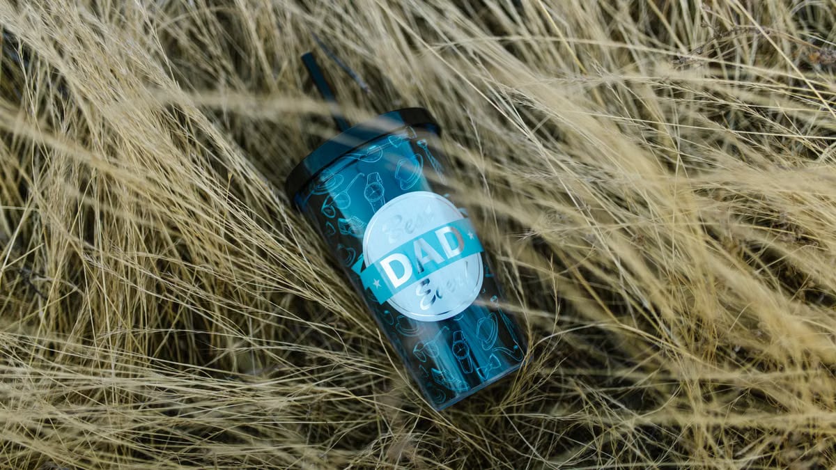 Eco-friendly reusable cup with 'DAD' label placed among dry grass outdoors.